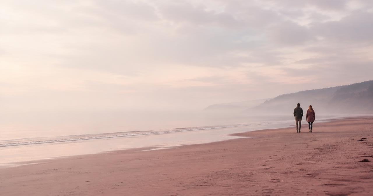 Zwei Menschen gehen in weichem Nebel gemeinsam am flachen Ufer entlang